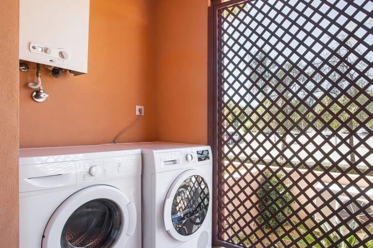 A laundry room with a washing machine and dryer and a boiler on top, How To Hide A Water Heater In The Laundry Room [9 Ideas To Inspire You!]
