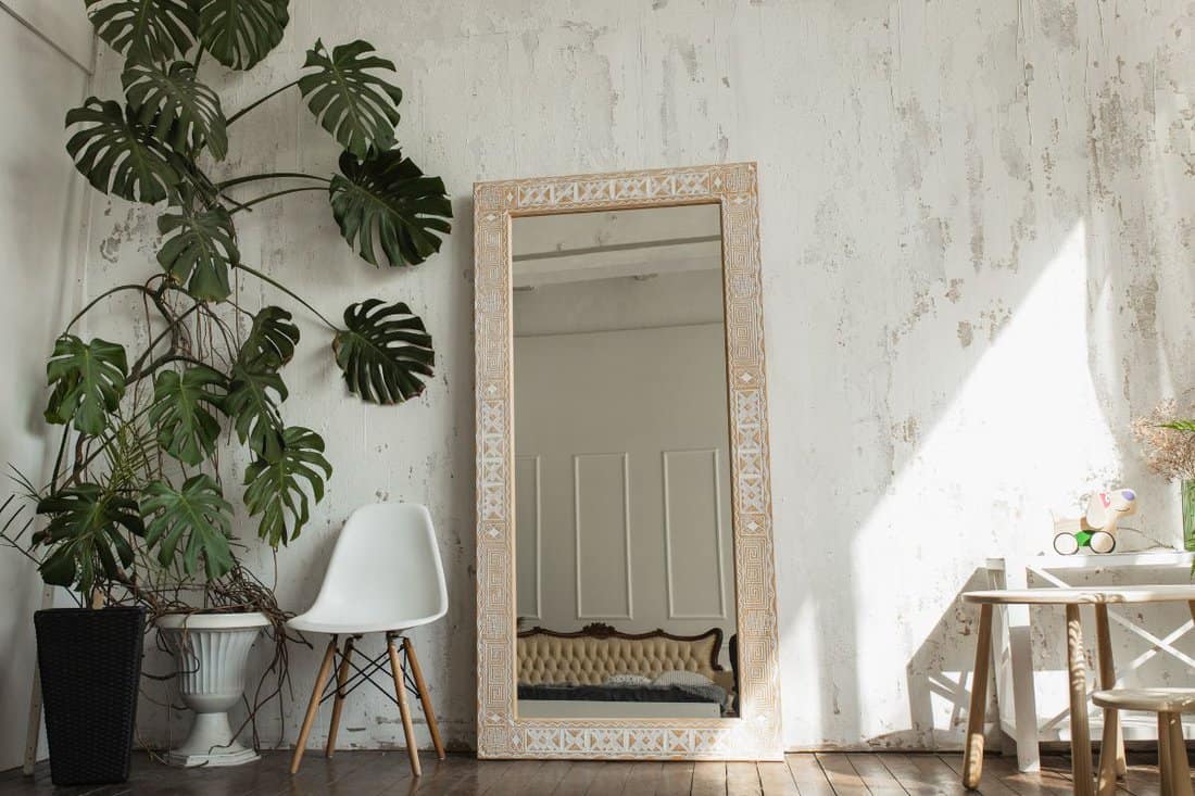Light brown wooden mirror with ethnic pattern in a bright room with white walls.