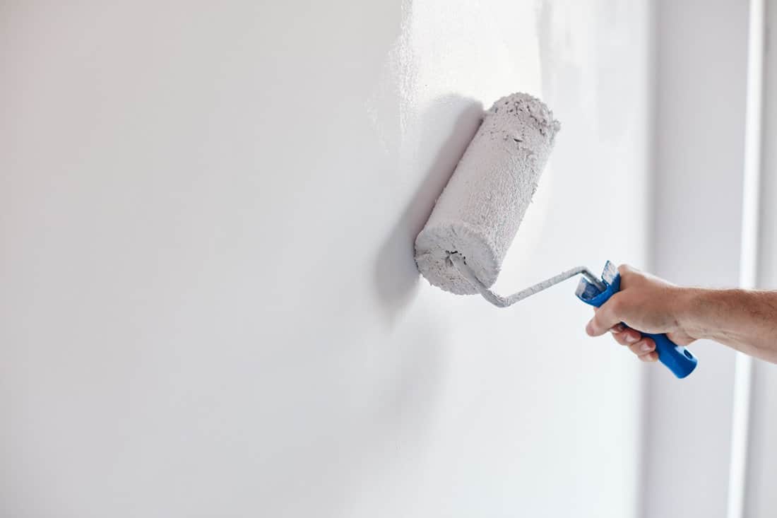Male hand painting wall with paint roller.