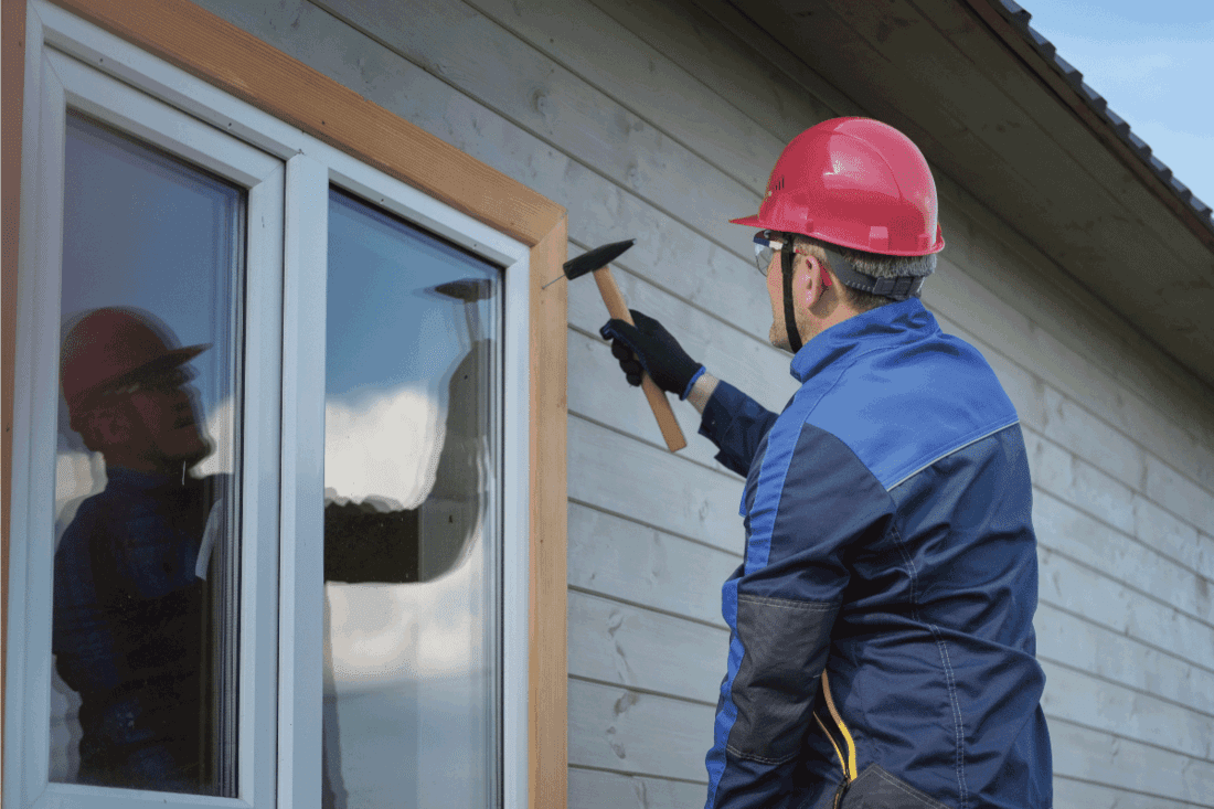 Man Builder in overalls performs installation of window trim. How Wide Should Window Trim Be