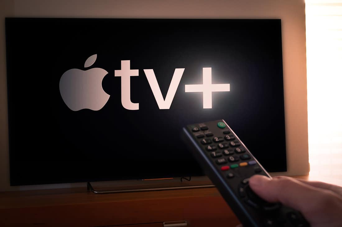 Man holds a remote control With the new Apple TV+ screen on TV. 