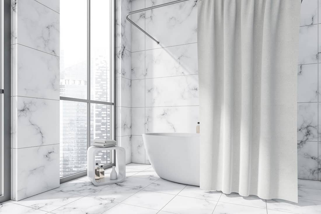 Modern bathroom interior, having an oval white ceramic bathtub with a curtain
