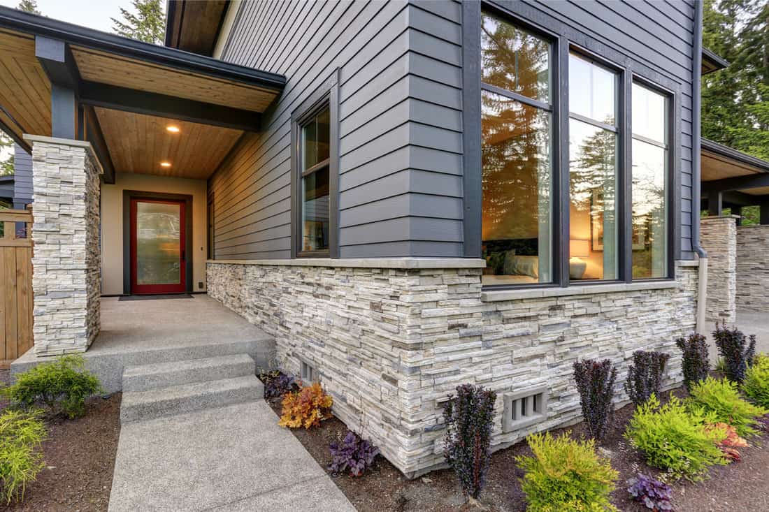 Modern luxurious house with stone veneer siding, gray wooden siding, and black framed windows