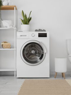 Modern washing machine, shelf unit and toilet bowl near white wall in bathroom interior, Can You Add A Toilet To A Laundry Room? [Yes, But Here's What You Need To Know!]