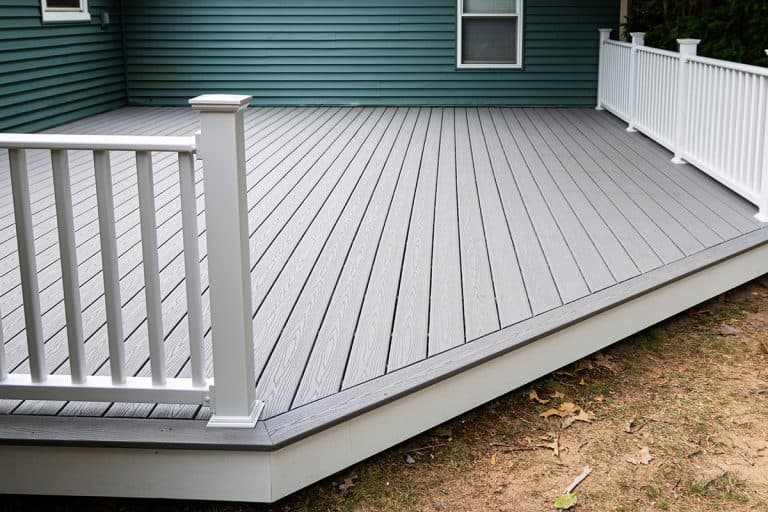 New composite deck on the back of a house with green vinyl siding with white railings, Should A Deck Railing Be Attached To The House?