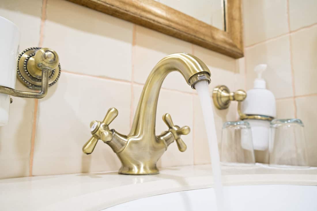 Open Retro faucet in bronze with a stream of water in the bathroom interior of the hotel 