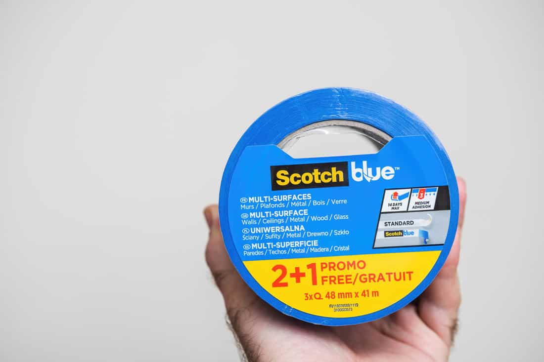 POV male hand holding new package with 3M professional painter's blue scotch for delicate surface