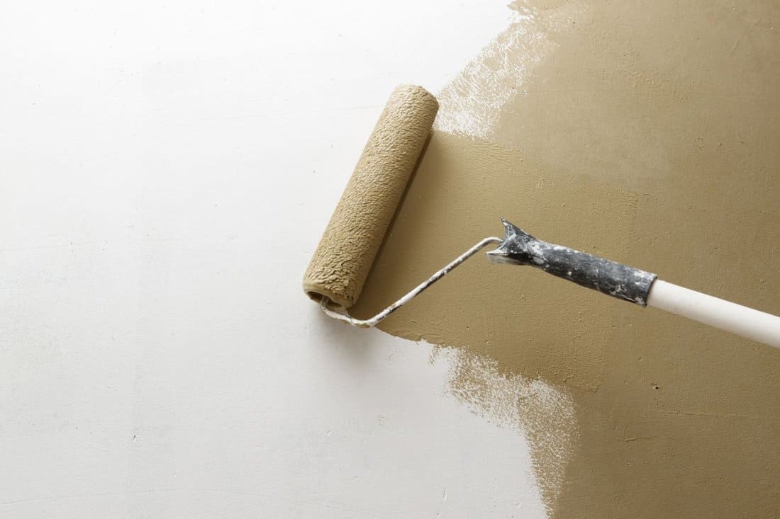 Paint roller applying brown paint on white wall, home improvements, horizontal view with copy space