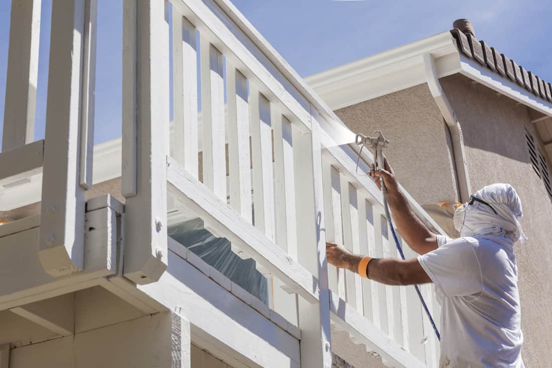 Painter spraying white paint on the wooden deck fence