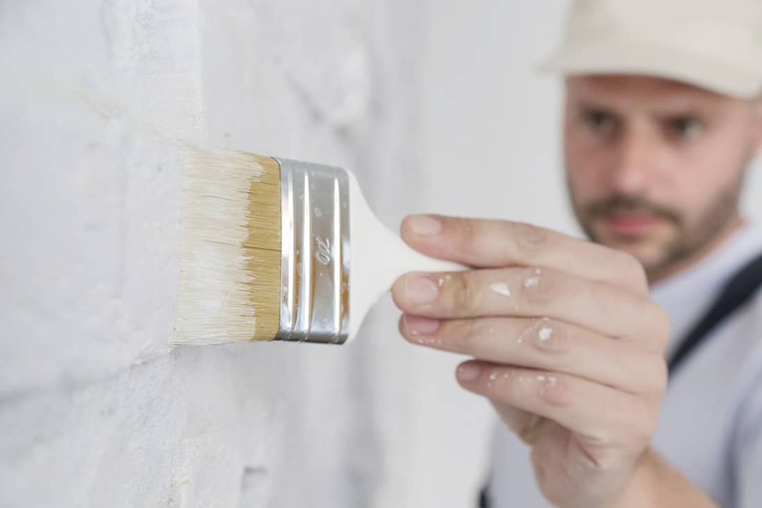 Painting a white brick wall with a paint brush.