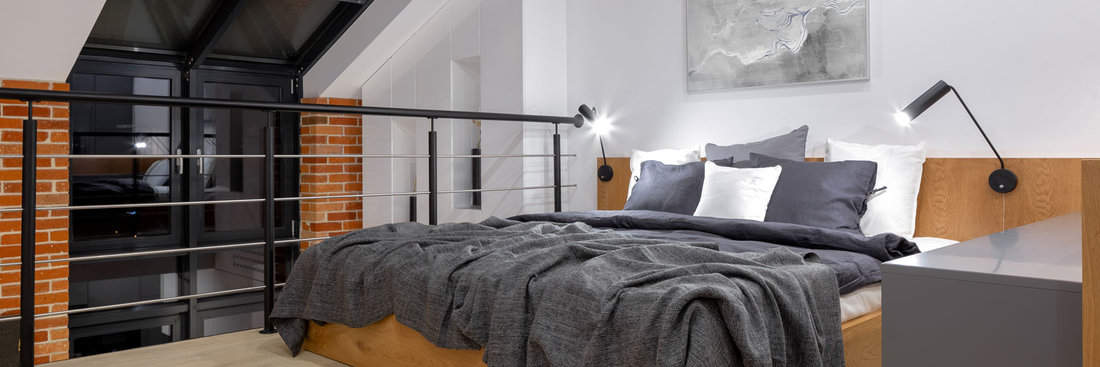 Panorama of modern bedroom on mezzanine in loft style apartment with big window and brick wall at night 