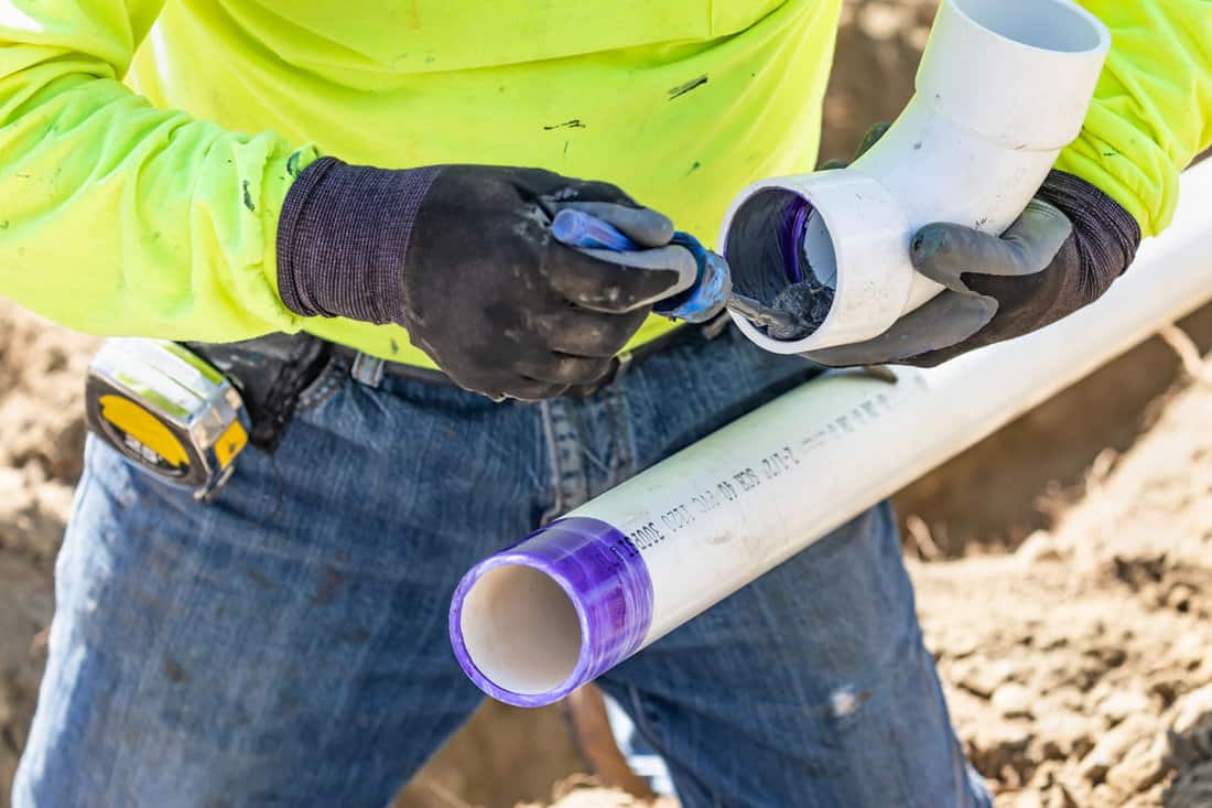 Plumber Applying Pipe Cleaner, Primer and Glue to PVC Pipe At Construction Site