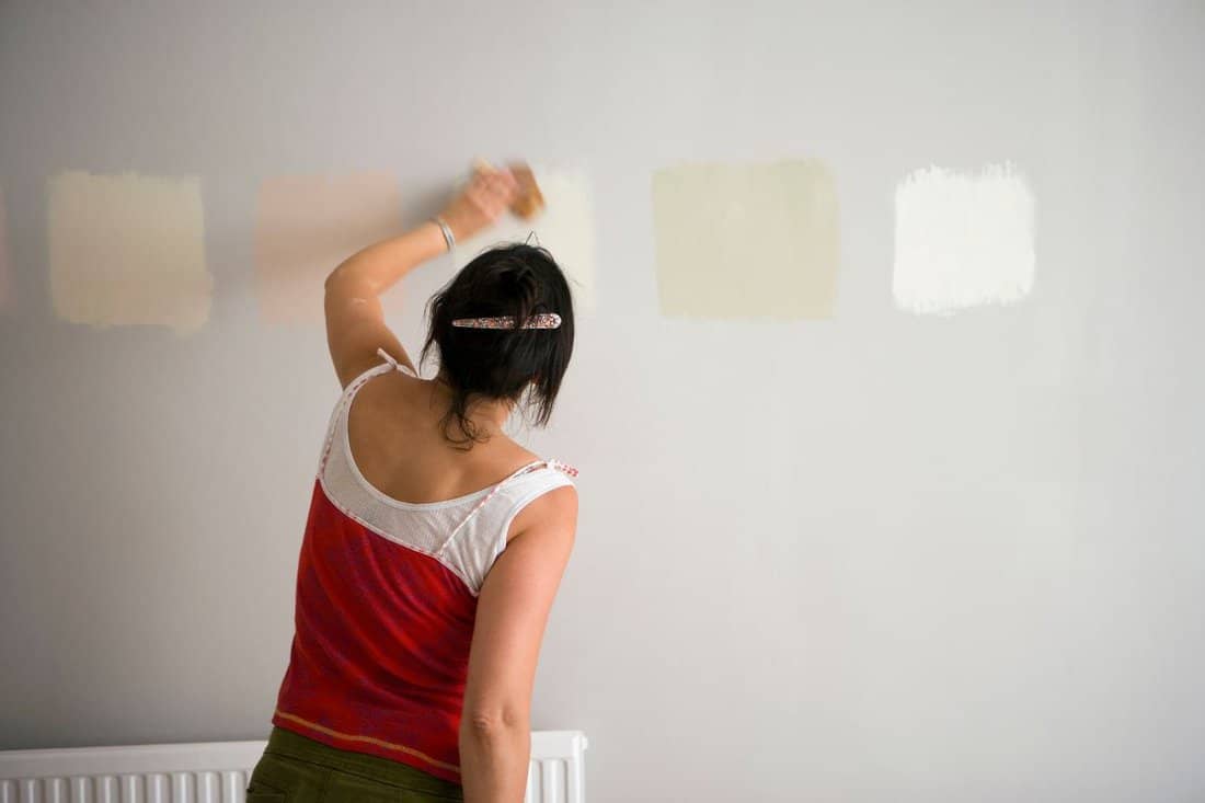 Rear view of a woman testing different paint shades over the wall.