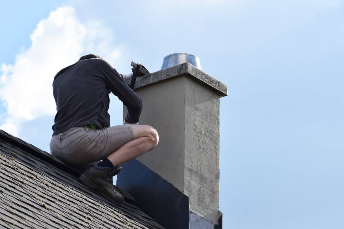 Roofer construction worker repairing chimney on grey slate shingles roof of domestic house