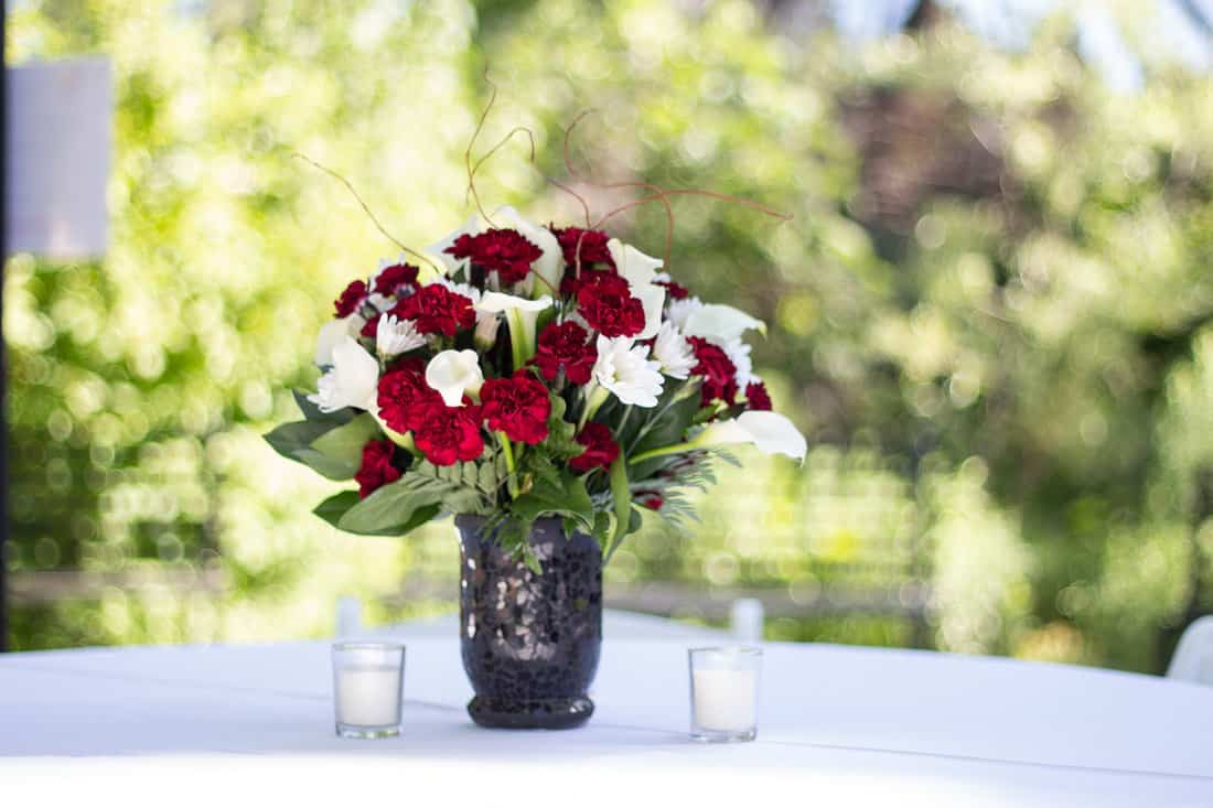 Tabletop floral centerpiece of deep red carnations, white daisies, calla lilies, and willow branches in a black vase, Elegant red and white floral centerpiece