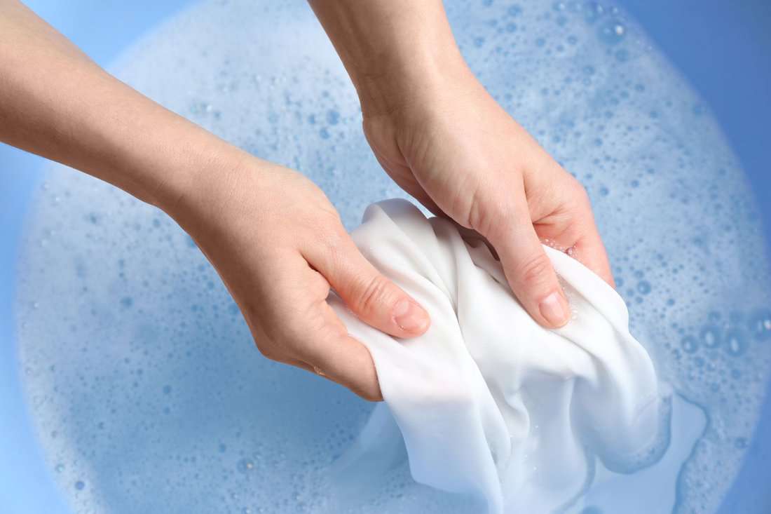 Top view of woman hand washing white clothing in suds, closeup