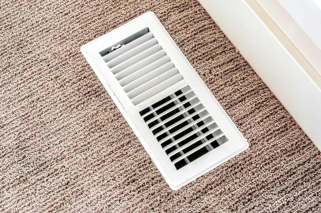 White air conditioner duct grille cover against floor with brown carpet 