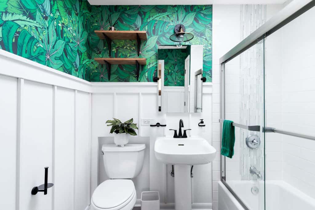White board and batten siding inside a narrow bathroom with green nature leaf wallpaper design
