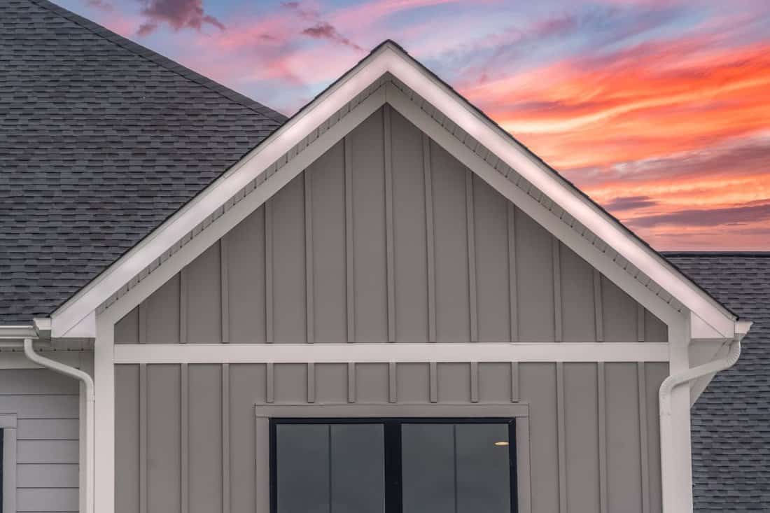 White frame gutter guard system, with dark gray horizontal vinyl siding, white accents, fascia, soffit, on a pitched roof attic at a luxury American single f