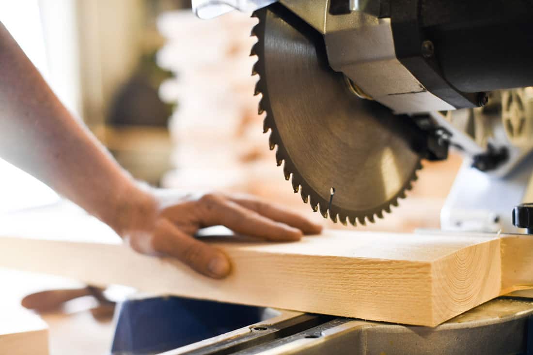 Worker hands details of wood cutter machine with a circular saw and wooden board