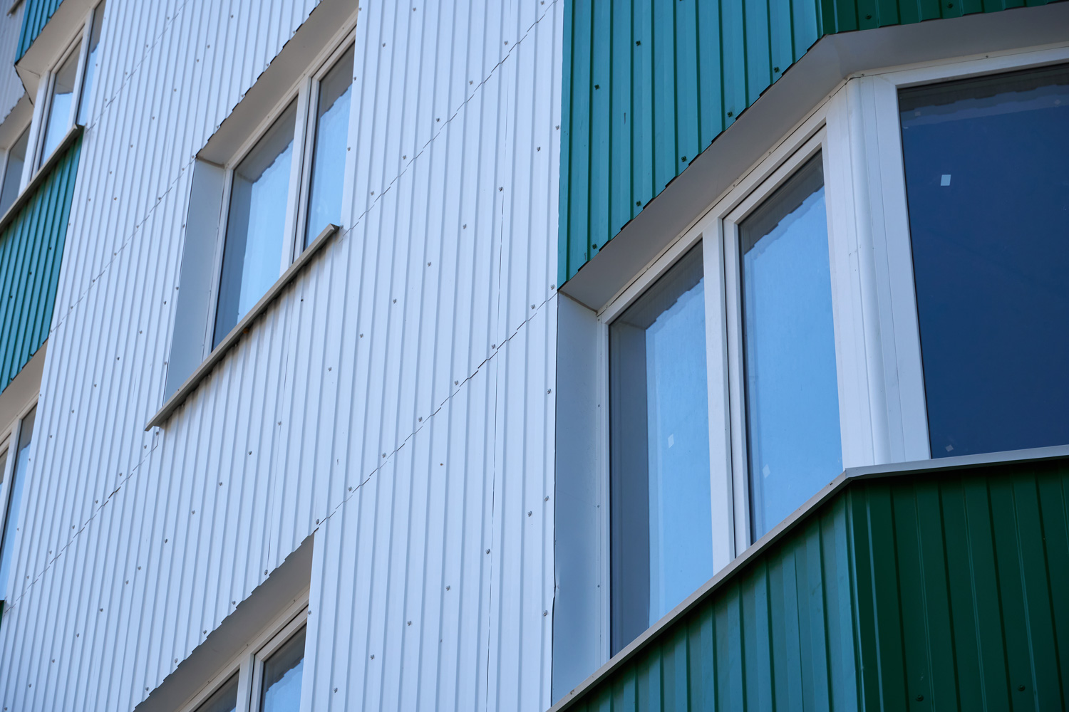 facade of a new multi-storey building with white and green metal siding, many Windows 
