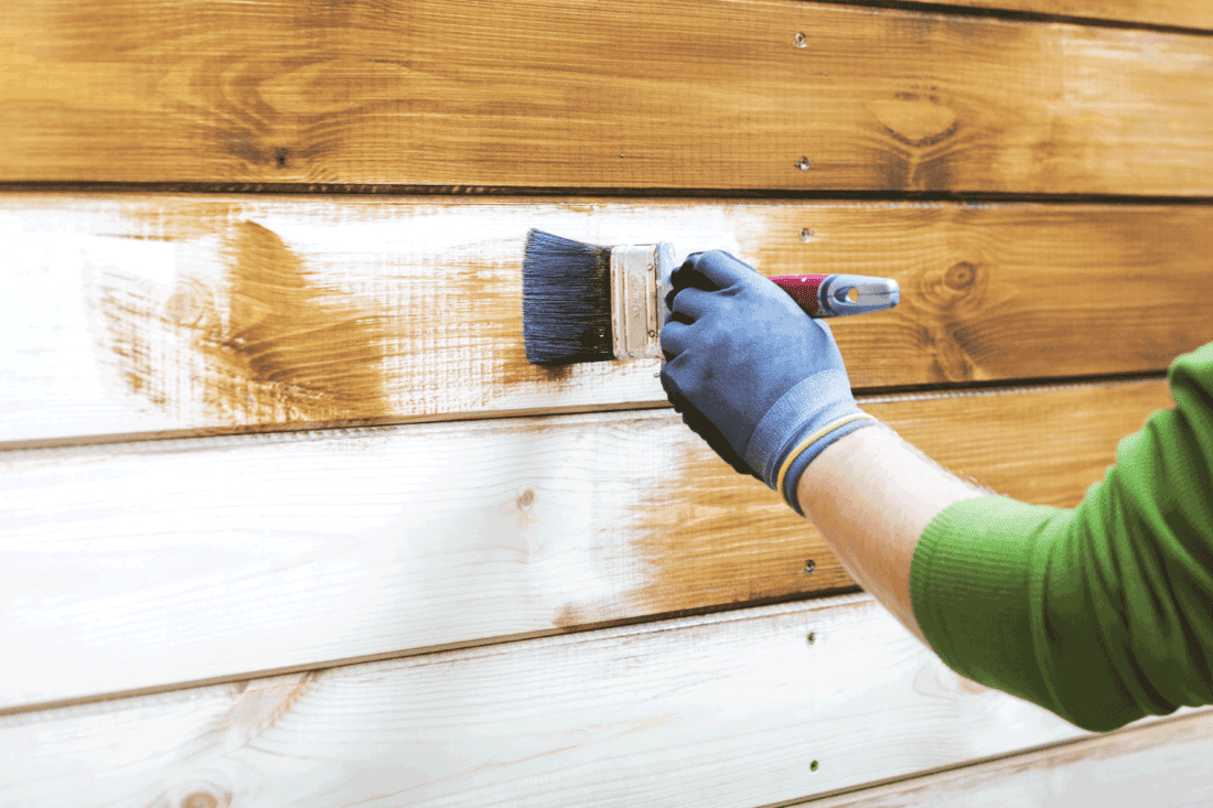 man painting wood house exterior siding with brown protective paint