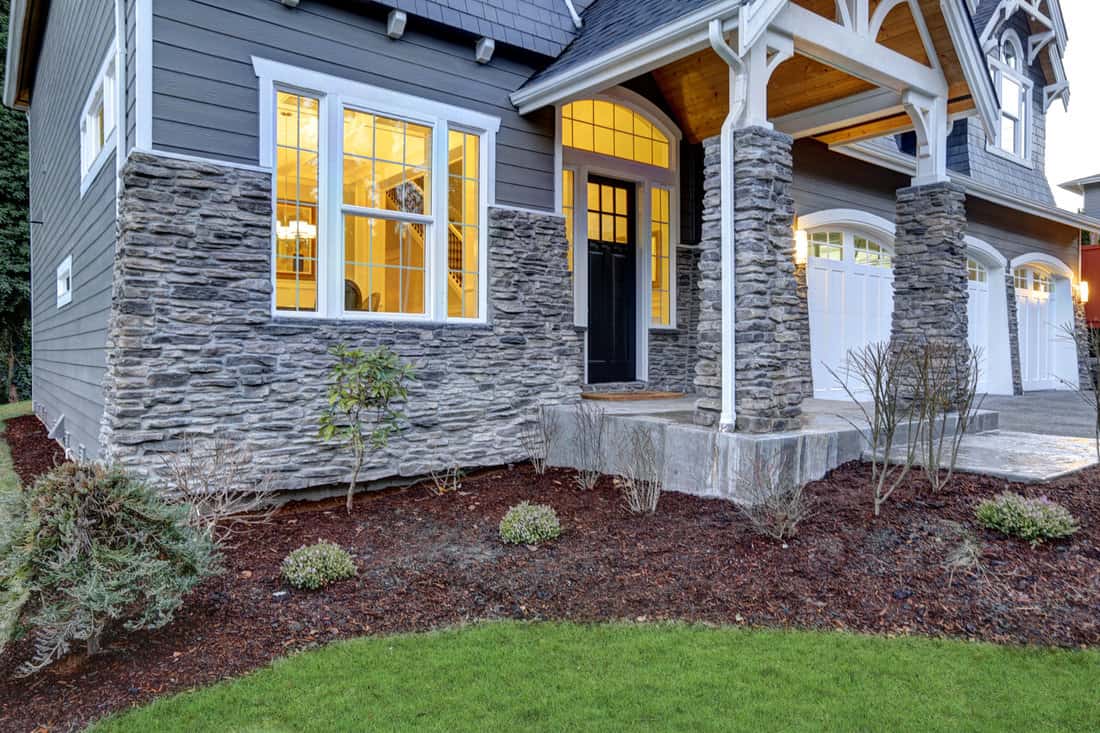 Front covered porch design boasts stone columns and rock siding that creates immense curb appeal of luxurious home. Northwest, USA 