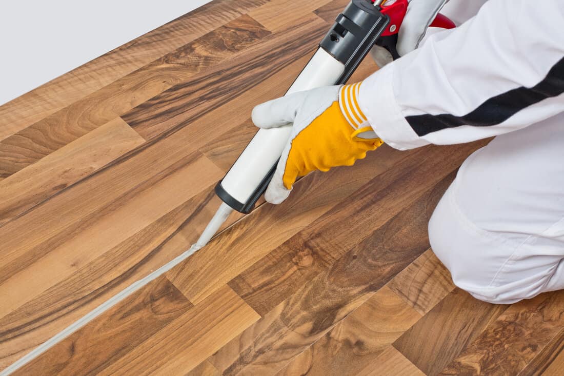 worker applies silicone sealant spaces of old wooden floor 
