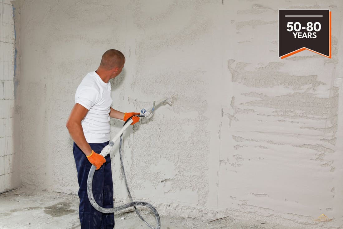 A man is applying stucco on the wall, plastering, coating the wall by spraying stucco with a stucco sprayer., At What Temperature Can You Apply Stucco?