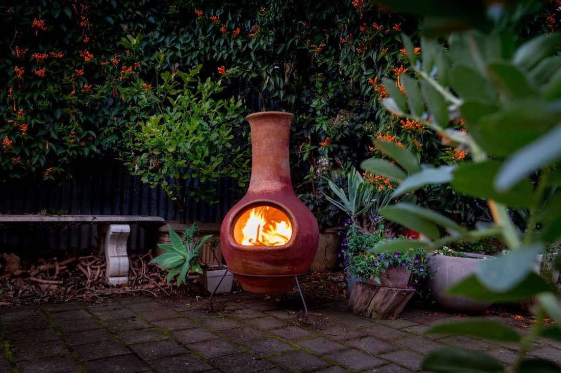 A Chimenea in the backyard. A backyard fire place surrounded by plants.
