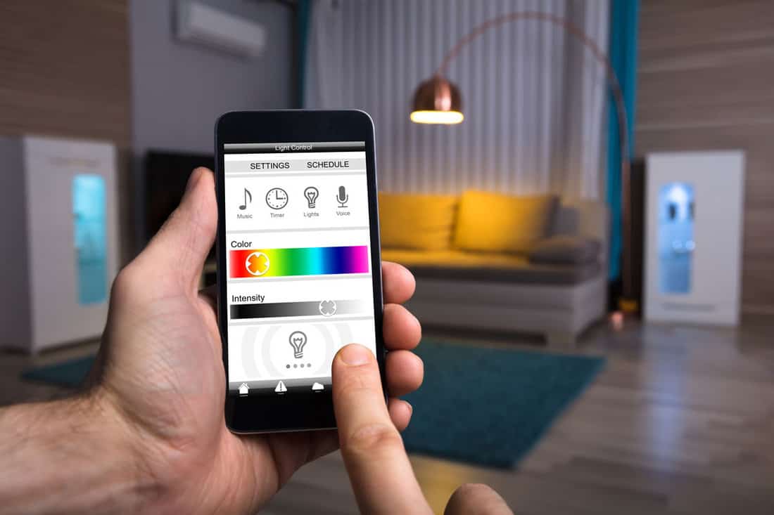 A Human Hand Adjusting Electric Light Through Mobile Phone At Home