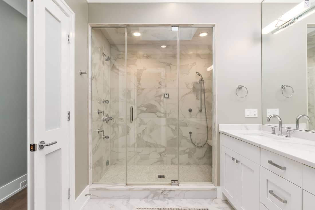 Modern bathroom with a white vanity, a marble tiled shower and glass door