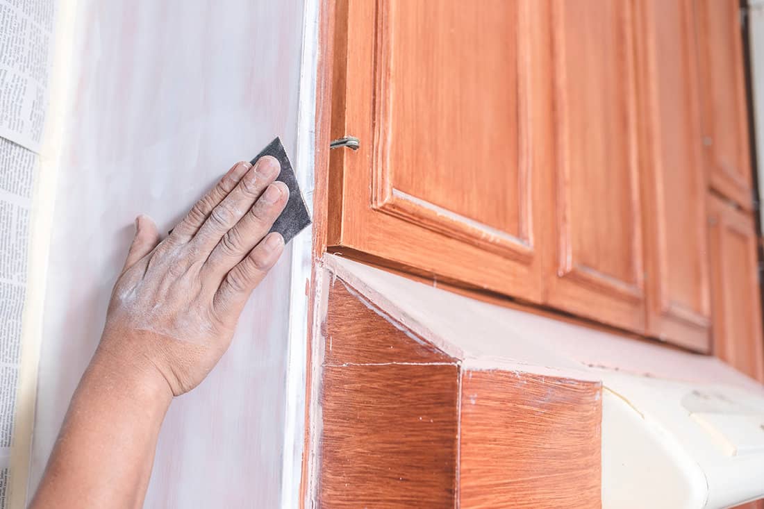 A handyman using a piece of sandpaper to smoothen out the edge of a wall cabinet prior to painting