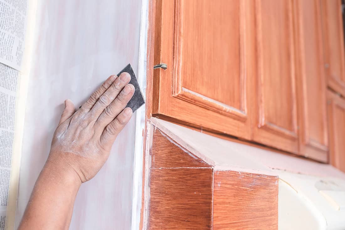 A handyman using a piece of sandpaper to smoothen out the edge of a wall cabinet
