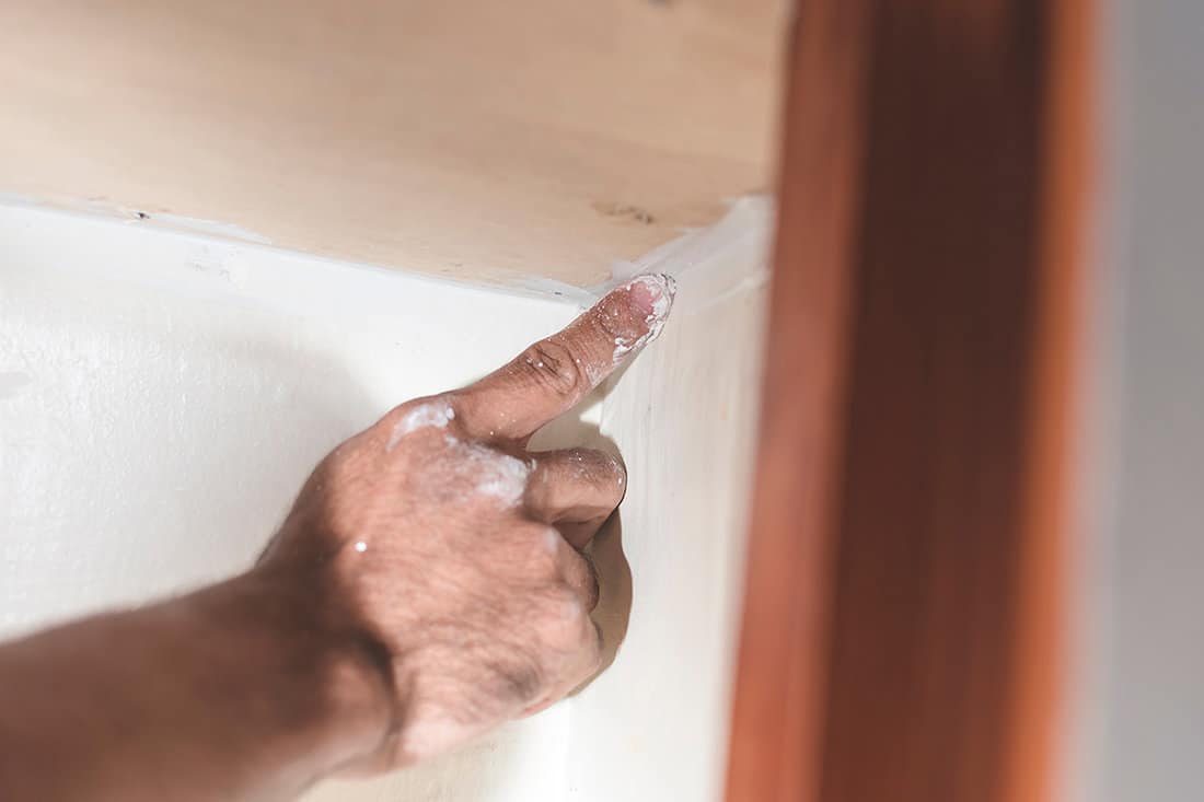 A man applies wood putty to the corner gaps inside the wall cabinet