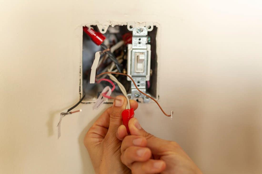 An electrician is replacing a wall switch. A DIY project concept. High voltage danger. She is working with bare hand tightening wires using plastic wirenut. There are labels on