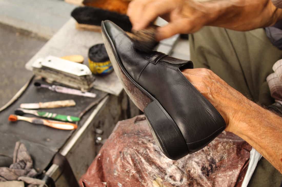 An old man hand polishing and painting a black shoe at stall