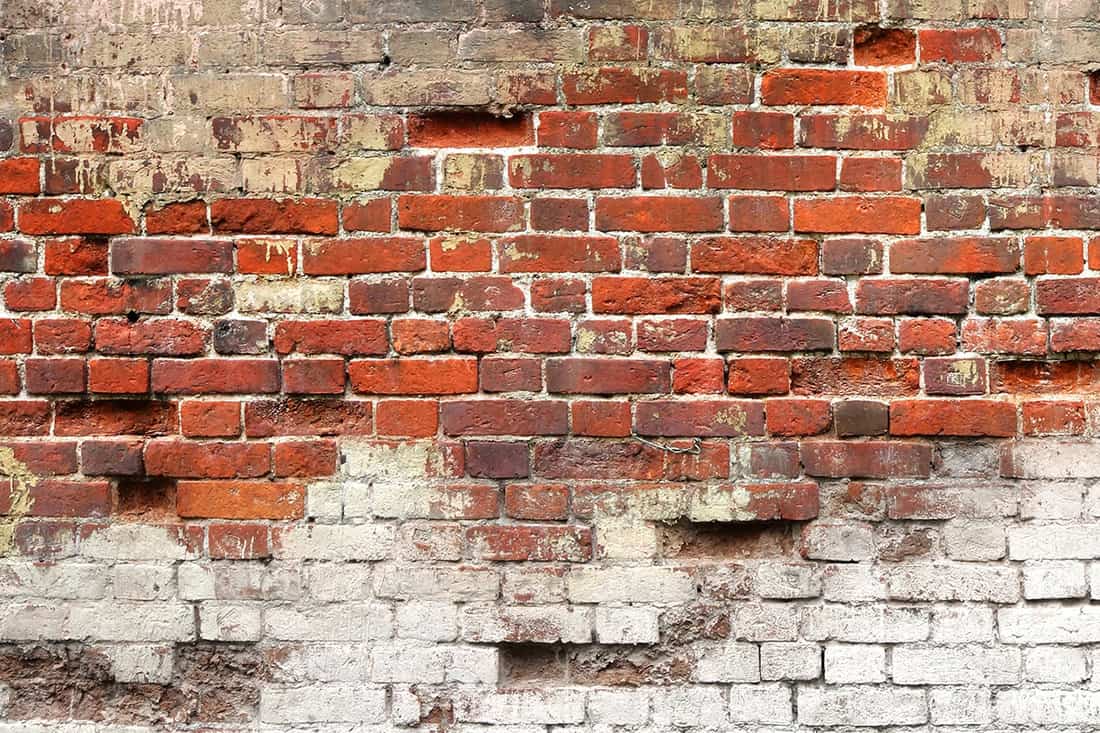 An uneven house wall with decayed old red and white bricks