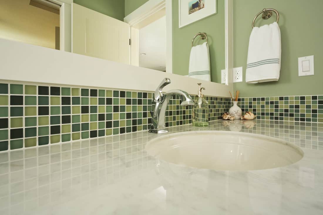 Bathroom sink of an upscale home/Horizontal shot of an elegant, polished and clean sink in an upscale home with colorful green tiling