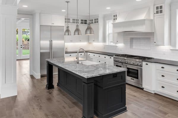 Beautiful Kitchen in New Luxury Home with Refrigerator, Oven, Hardwood Floors, Kitchen Island, and Pendant Lights, Is Granite Cheaper Than Quartz? [Which Is Better?]