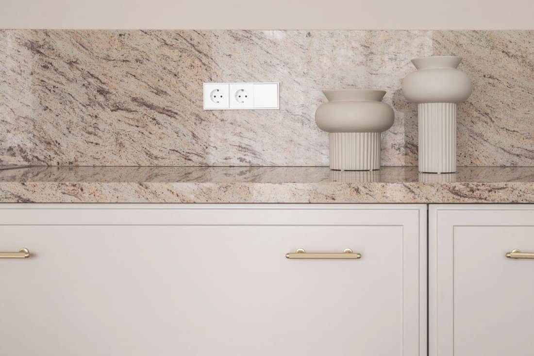 Beige granite kitchen counter with electric outlets on stone wall, two elegant beige vases