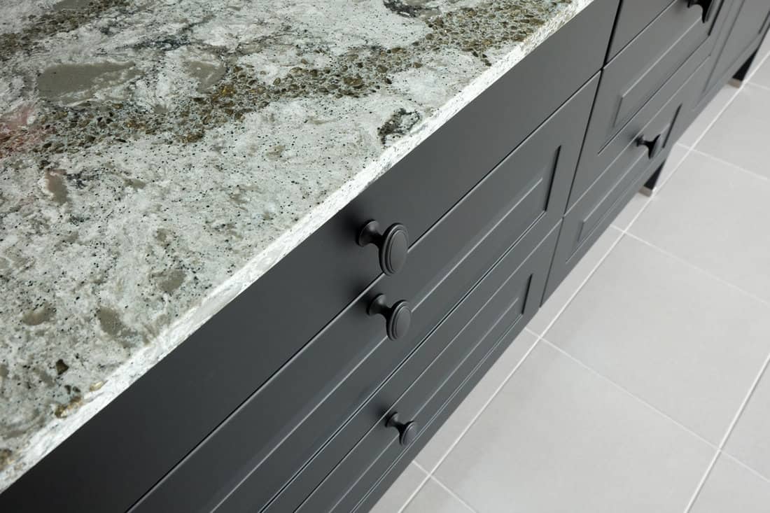 Black metal handles on wooden drawer and front door of kitchen cabinet under stone worktop .