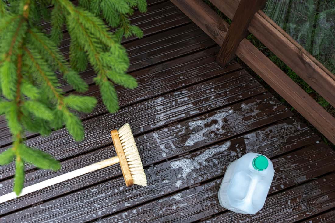 Brush and plastic canister with detergent on a wooden board, wooden terrace