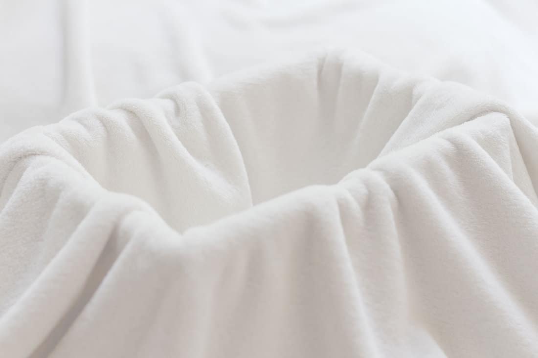Cozy and comfortable look of white clean fleece blanket or throw with rectangular basket underneath making containable space background. Selective focus and shallow depth of field. 