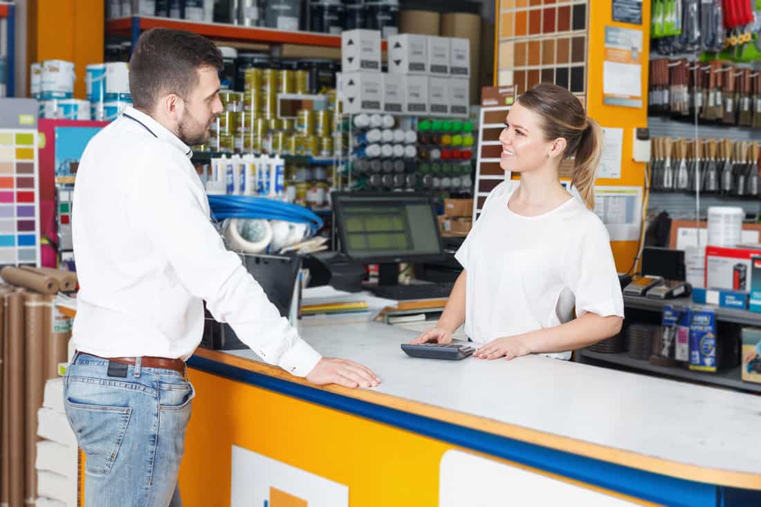 Cheerful girl seller helping male customer at the counter in shop 