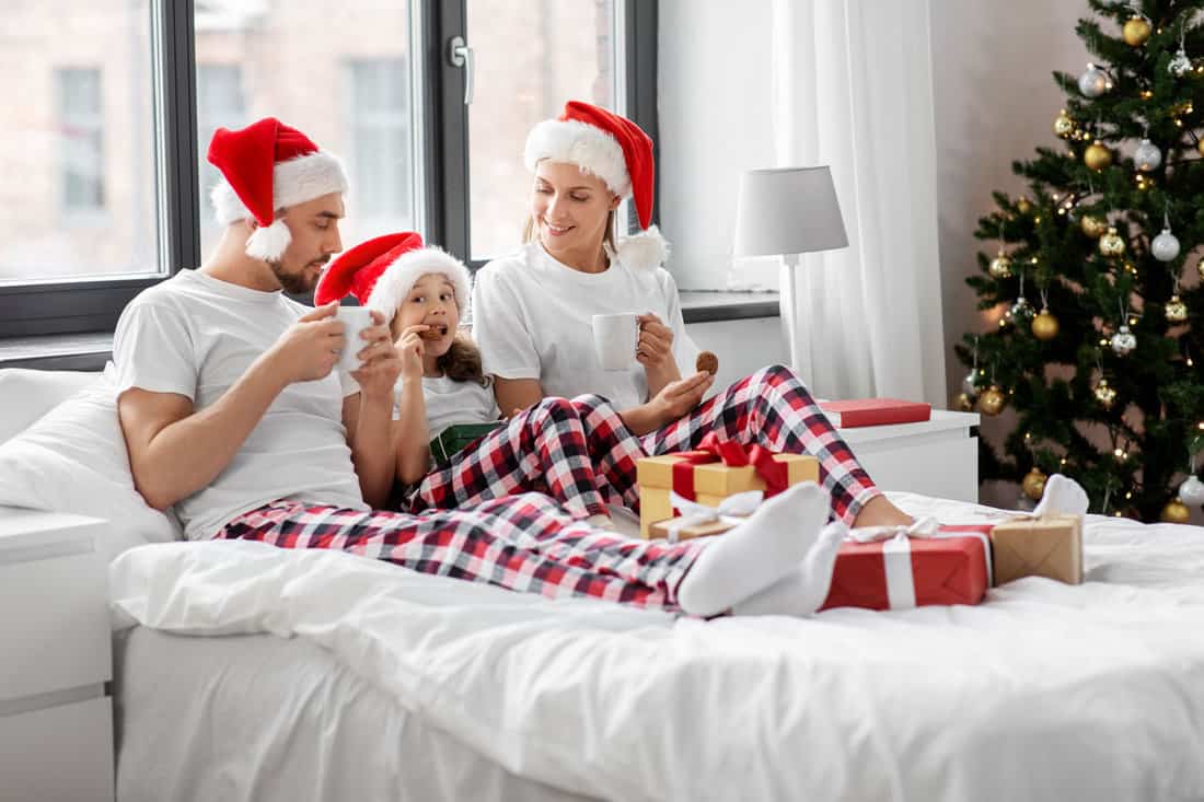 family, winter holidays and people concept - happy mother, father and little daughter with christmas gifts drinking coffee and eating coookies in bed at home 