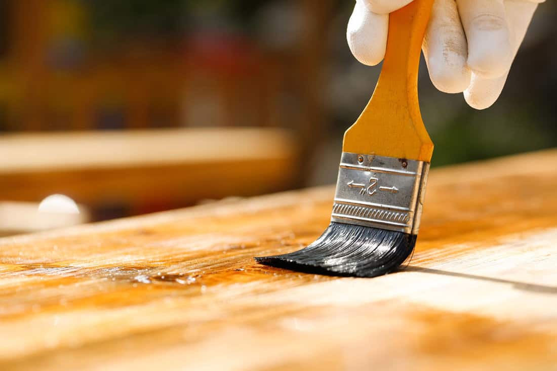 Gloved hand holding a paintbrush over wooden surface, protecting wood for exterior influences and weathering