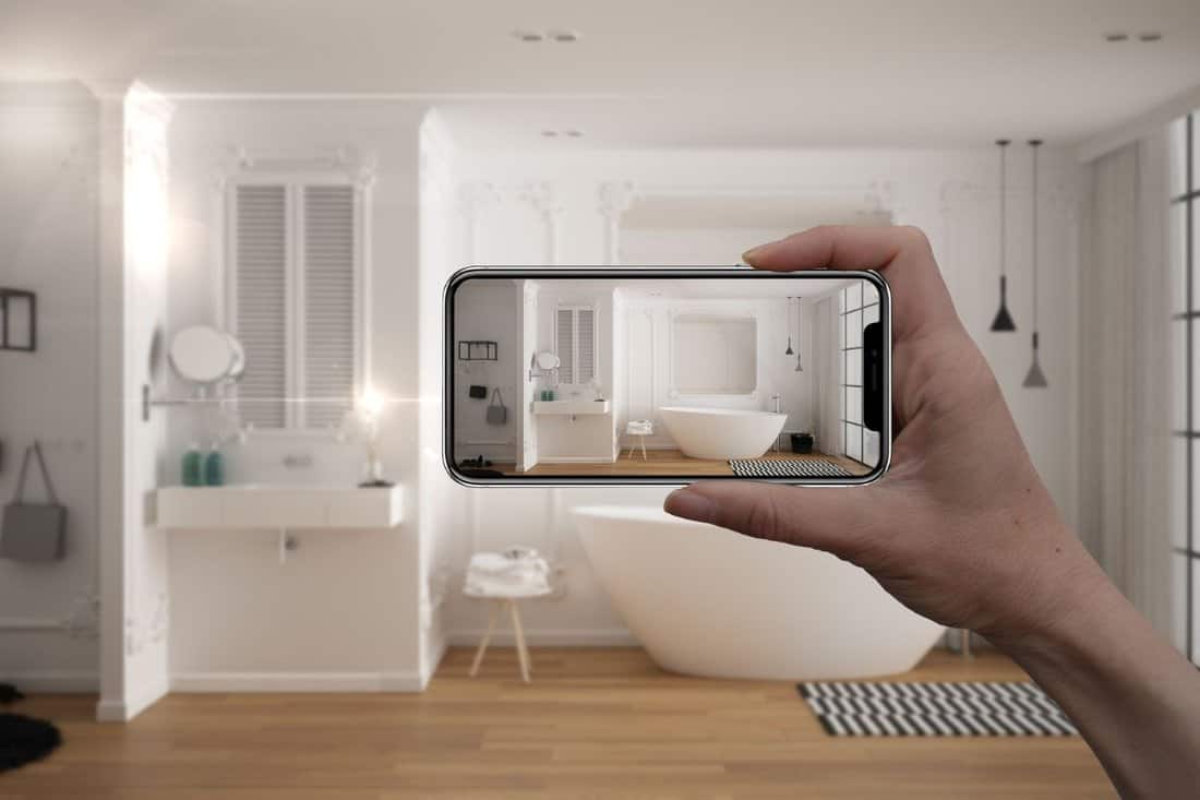 Hand holding smart phone, AR application, simulate furniture and interior design products in real home, architect designer concept, blur background, minimalist bathroom with bathtub