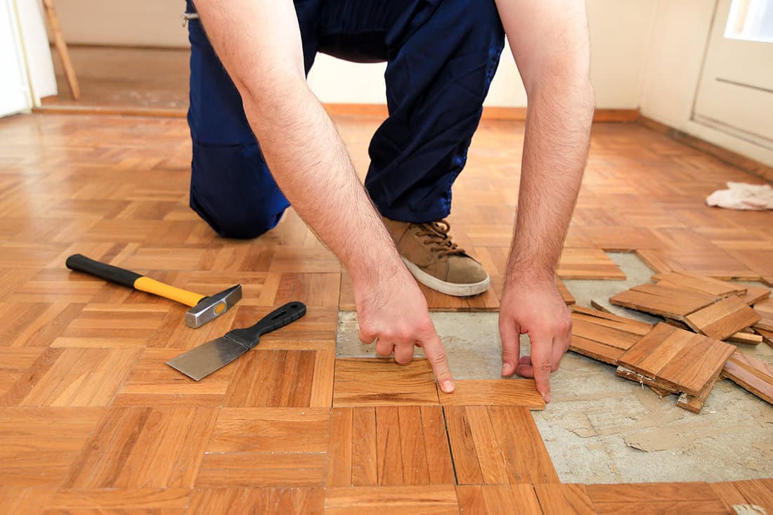 Handyman is removing old wooden parquet flooring using yellow hammer and scraping tool