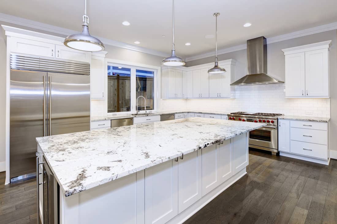 Large, spacious kitchen design with white kitchen cabinets, white kitchen island with lots of storage, white Granite countertops, subway tiles and stainless steel appliances. 